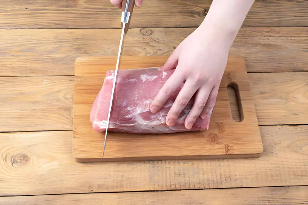 cutting raw pork meat with a kitchen knife