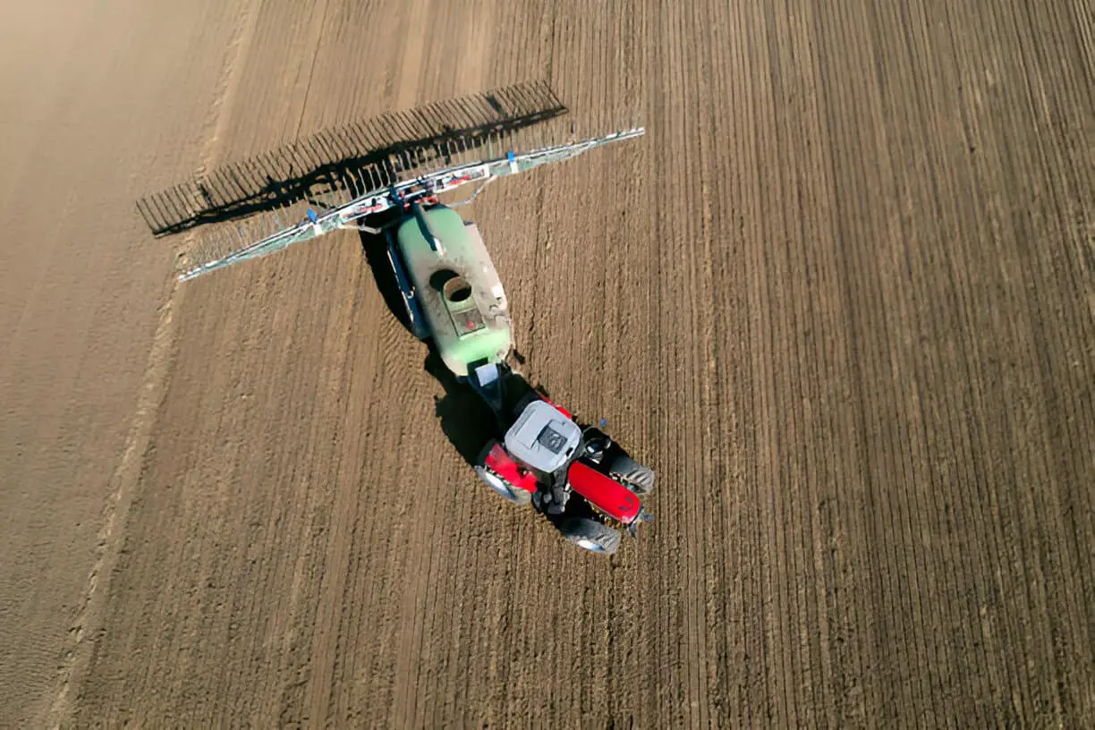 a red tractor fertilizing field